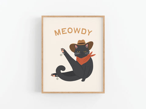 Meowdy Cat Art Print by Onderkast Studio features a black cat in a cowboy hat and red bandana raising one leg under the word MEOWDY—a playful framed print for cat lovers, perfect for brightening up any space.