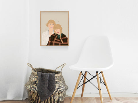 The TS Folkevermore Art Print by Onderkast Studio hangs on a white wall above a woven basket and beside a modern chair, adding cozy woodsy charm and folklore-inspired style to the bright, minimal room.