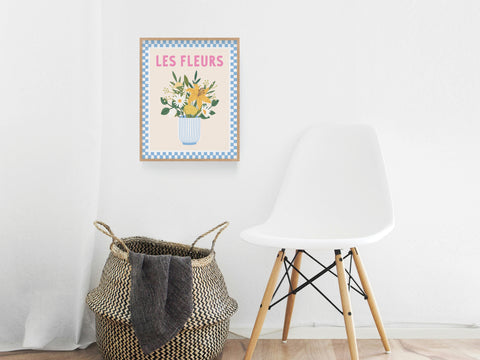 A minimal room with a white chair, a woven basket holding a dark towel, and the Les Fleurs Art Print by Onderkast Studio—Parisian elegance framed in blue checks—hangs on a crisp white wall.