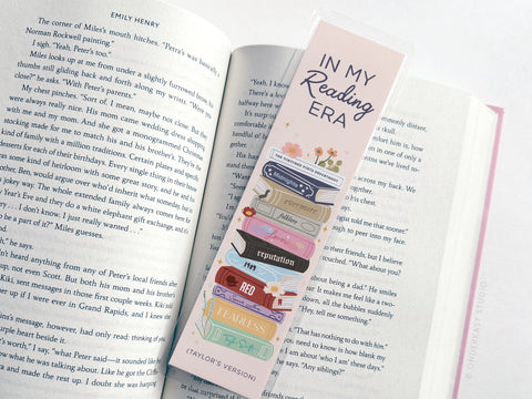 The TS In My Reading Era Laminated Bookmark by Easyhand Goods features vibrant print, an In My Reading Era message, and a stack of books titled with Taylor Swift albums like Red, Reputation, and Fearless (Taylor’s Version).