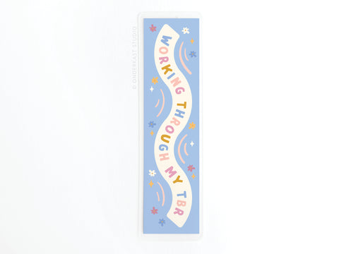 The Working Through My TBR Laminated Bookmark by Easyhand Goods features colorful, wavy lettering on a light blue background with whimsical stars and swirls—an ideal, sturdy accessory for any book lovers reading adventures.