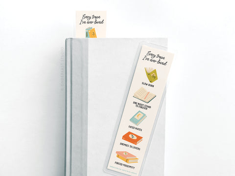 The Every Trope Ive Ever Loved Laminated Bookmark by Easyhand Goods features icons for romance tropes like slow burn, enemies to lovers, and fated mates—a perfect accessory for book lovers. Comes with a matching sticky note and a white and light gray book.