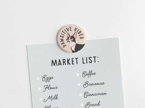 The Onderkast Studio Pawsitive Vibe Dog Button Magnet holds a shopping list (eggs, flour, milk, coffee, bananas, cinnamon, and bread) on a light grey surface.