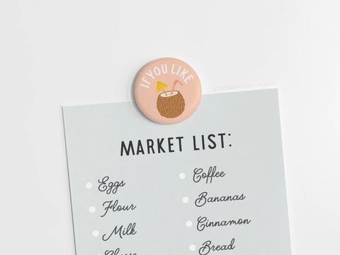 The If You Like Piña Coladas Button Magnet by Onderkast Studio features a round pink design with a coconut drink and holds your market list—perfect for cocktail lovers or any tropical magnet collection.