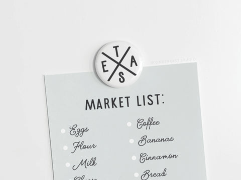 A light blue shopping list with items like eggs, flour, and milk is attached to a white surface using the Onderkast Studio Texas Logo Button Magnet.