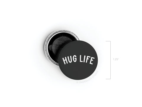 The Hug Life Button Magnet by Onderkast Studio features bold white text on a round black surface. Measuring 1.25 in diameter, this magnet and its silver backing make a charming, compact addition to your space or collection.