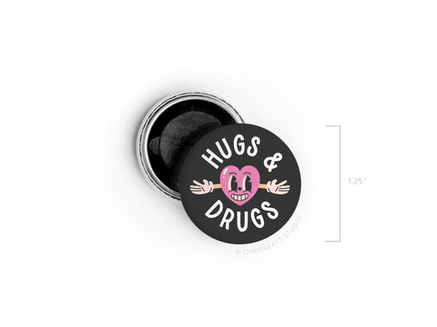 The Hugs & Drugs Button Magnet by Onderkast Studio features a round black design with a pink cartoon heart and HUGS & DRUGS text. At 1.25 inches diameter, its metallic back is visible—perfect for fans of Physical Touch.
