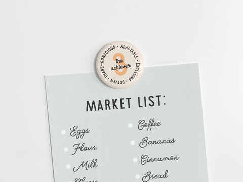 A grocery list is held by the Onderkast Studio Enneagram Button Magnet – 3 The Achiever, perfect for driven, adaptable Type 3s.