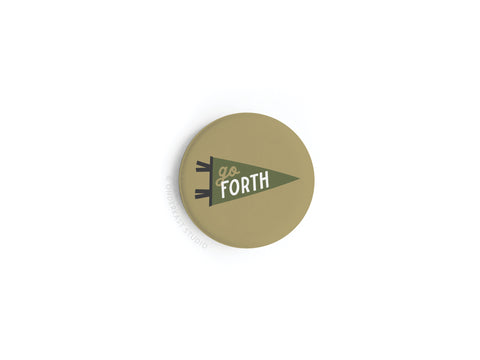 The Go Forth Button Magnet by Onderkast Studio is round and beige, featuring a green pennant with “go FORTH” in white and green letters. It boasts high-quality production and vibrant colors on a plain white background.