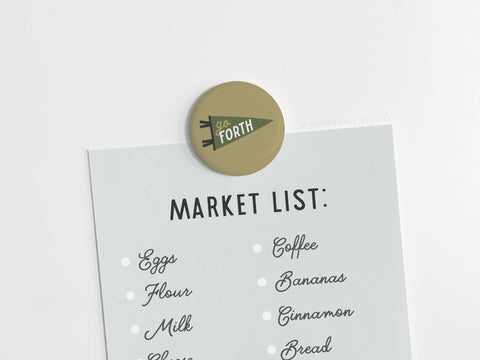 A market list is held to any surface by the Onderkast Studio Go Forth Button Magnet, whose vibrant colors add flair as you jot down essentials like eggs, flour, milk, coffee, bananas, cinnamon, and bread.