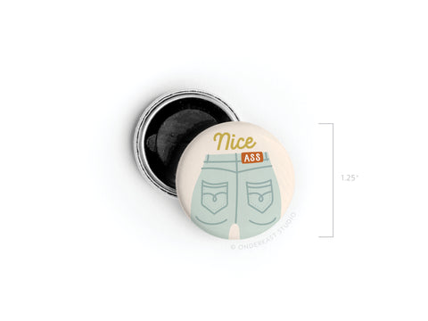 The Nice Ass Button Magnet by Onderkast Studio features an illustration of jean-clad buttocks with “Nice Ass” text, perfect for celebrating self-love and body confidence. Measures 1.25 inches; lid shown open beside it.