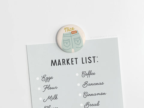 The Nice Ass Button Magnet by Onderkast Studio, with jean pockets and Nice Ass text, adds body confidence to your space while holding your market list—eggs, flour, milk, coffee, bananas, cinnamon, bread—on any white surface.