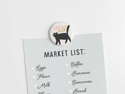 The Bad Luck Club Button Magnet by Onderkast Studio is a round magnet with a black cat and Bad Luck Club design, perfect for holding your grocery list on any white surface.
