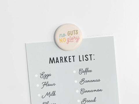 The Onderkast Studio No Guts No Glory Button Magnet holds your grocery list to a white surface, offering motivation as you shop for essentials like eggs, milk, flour, bananas, cinnamon, and bread.