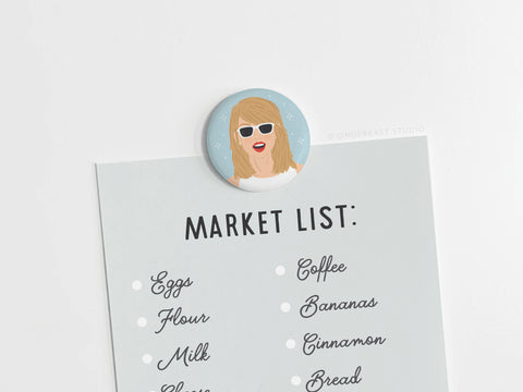 The Onderkast Studio TS 1989 Button Magnet features a cartoon woman in sunglasses with a blue Market List of groceries—a playful tribute to pop perfection and Taylors iconic album.