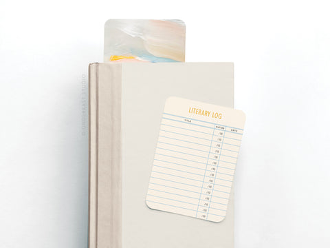 The Onderkast Studio Literary Log Book Review Card Set features a closed beige book with a bookmark and a blank review card on its cover, photographed against a white background.