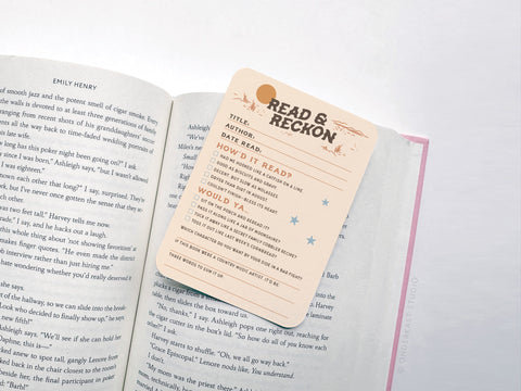 The Read & Reckon Book Review Card Set by Onderkast Studio includes peach-colored cards printed on premium cardstock with vibrant colors, readability rating checkboxes, and a “Would Ya Recommend?” section featuring star and moon illustrations.