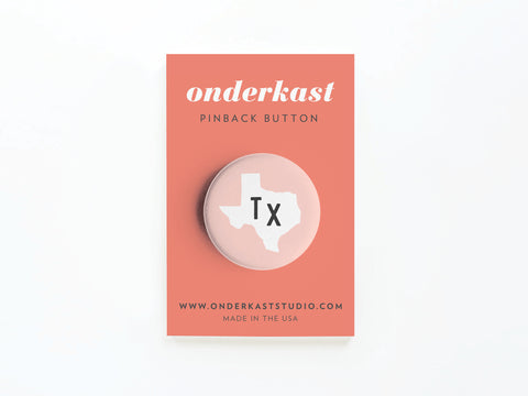 Show your Texan style with the Light Pink TX Pinback Button by Onderkast Studio—featuring a white Texas outline and black Tx, displayed on a coral Onderkast PINBACK BUTTON card, with website and MADE IN THE USA at the bottom.