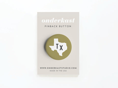 A round Green TX Pinback Button by Onderkast Studio features a white Texas outline with Tx in black, displayed on a beige Onderkast PINBACK BUTTON card. Proudly MADE IN THE USA, with website at the bottom.