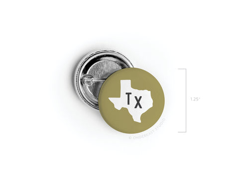 The Green TX Pinback Button by Onderkast Studio features a bold black TX and white Texas shape on a light olive-green background. Measuring 1.25, this accessory is proudly printed in the USA and captures signature Texan style.
