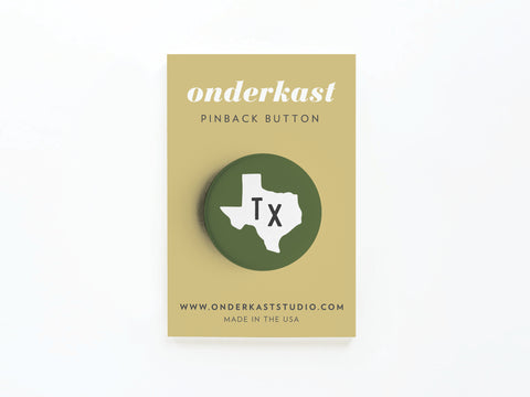 The Dark Green TX Pinback Button by Onderkast Studio features a white Texas outline and Tx text. Its attached to a tan card labeled ONDERKAST PINBACK BUTTON with state pride details, website info, and Printed in USA at the bottom.