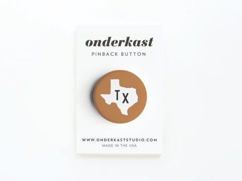 Show your state pride with the Brown TX Pinback Button from Onderkast Studio—featuring a white Texas shape and black Tx letters on brown, displayed on a branded Onderkast pinback card. Made in the USA.