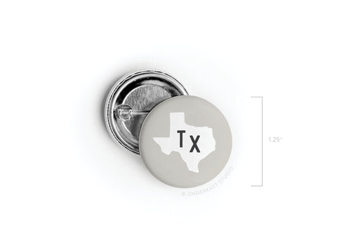 The Onderkast Studio Gray TX Pinback Button features a light gray background with a white Texas outline and bold black Tx. Measuring 1.25 in diameter, this button is perfect for showcasing your state pride.