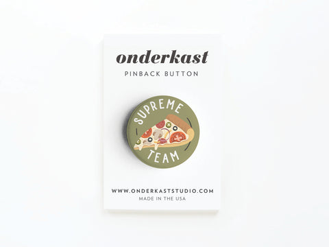 The Supreme Team Pizza Pinback Button by Onderkast Studio features a pizza slice design and SUPREME TEAM text, making it ideal for pizza lovers. It comes attached to an Onderkast Studio card displaying their website and MADE IN THE USA.