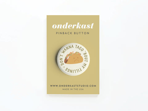 The Don’t Wanna Taco ‘Bout It Pinback Button by Onderkast Studio features a sad taco and funny text—a great gift for taco lovers. Comes on a tan card labeled “Onderkast PINBACK BUTTON” with www.onderkaststudio.com, MADE IN THE USA.