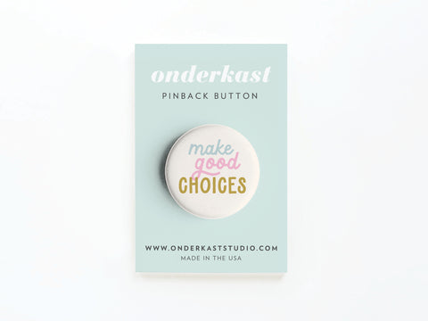 The Make Good Choices Pinback Button by onderkast studio features “make good CHOICES” in pastel pink, yellow, and white on a round pinback button with a card reading “onderkast PINBACK BUTTON” and the website www.onderkaststudio.com. Made in the USA.