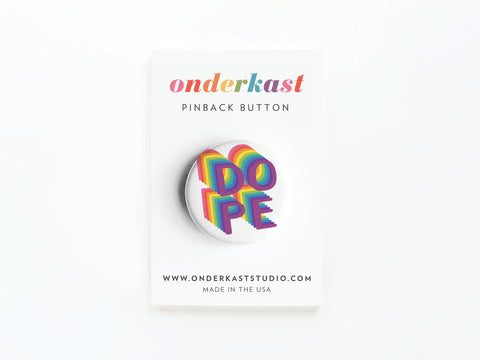 The DOPE Pinback Button by Onderkast Studio features bold, rainbow 3D lettering and comes attached to a branded Onderkast card with product name, website, and origin details displayed below.