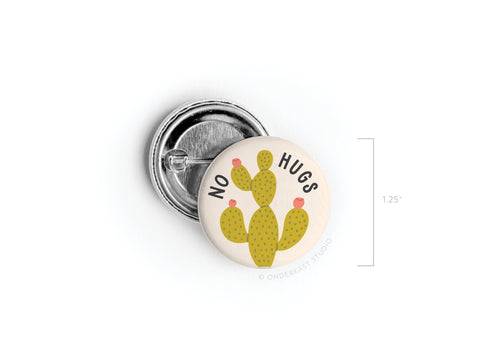The No Hugs Cactus Pinback Button by Onderkast Studio is a 1.25-inch beige accessory featuring an illustrated cactus with NO HUGS above it—great for introverts who love playful flair.
