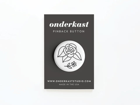 The Black Flowers Pinback Button by Onderkast Studio features a simple black line rose and leaf design on a round button, attached to branded carding with onderkaststudio.com, and is printed in the USA.