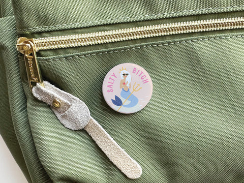 The Salty Bitch Mermaid Pinback Button by Onderkast Studio features a cartoon mermaid and playful text, making it the perfect accessory for ocean lovers and beach babes.