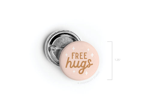 The Free Hugs Pinback Button by Onderkast Studio features bold, playful lettering on a pink background with white stars. This 1.25-inch round button comes with a metal pin backing for easy attachment to your bag or jacket.