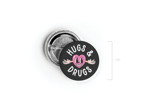 The Onderkast Studio Hugs & Drugs Pinback Button features a smiling pink heart with arms on a black background, vibrant colors, and HUGS & DRUGS text. Measures 1.25 inches.