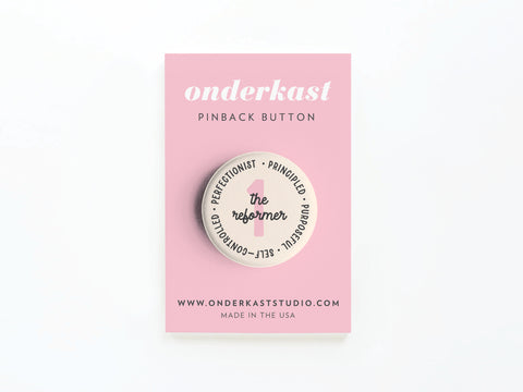 The Enneagram Pinback Button – 1 The Reformer by Onderkast Studio features traits like principled, purposeful, self-controlled, and perfectionist—perfect for fans of self-improvement. Presented on a pink card labeled onderkast PINBACK BUTTON.