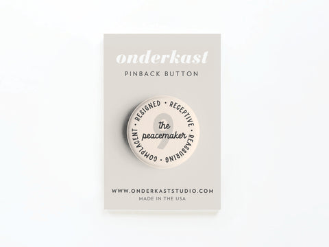 The Enneagram Pinback Button – 9 The Peacemaker by Onderkast Studio rests on a beige card with traits like receptive and reassuring, onderkast PINBACK BUTTON, and MADE IN THE USA plus website text below.