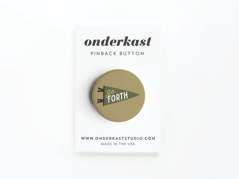 The Go Forth Pinback Button by Onderkast Studio is round, olive-green, and features a triangular flag design. Attached to an Onderkast PINBACK BUTTON card with the website and MADE IN THE USA printed at the bottom.