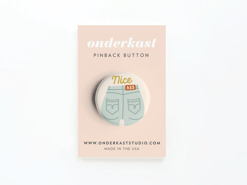 The Nice Ass Pinback Button by Onderkast Studio features Nice Ass! above jean shorts back pockets, celebrating self-love and body confidence. Card includes www.onderkaststudio.com and Made in the USA.