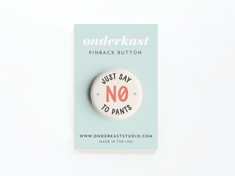 The Just Say No to Pants Pinback Button by Onderkast Studio features Just Say No to Pants with NO in bold red, celebrates a pants-free lifestyle, and comes on a light blue display card with branding and website info.
