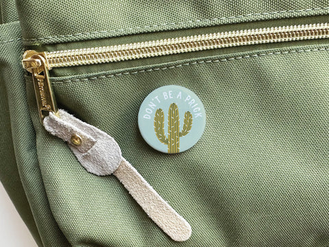 Add a playful touch with the Onderkast Studio Don’t Be a Prick Pinback Button, featuring a cactus and bold white lettering—perfect for any bag.