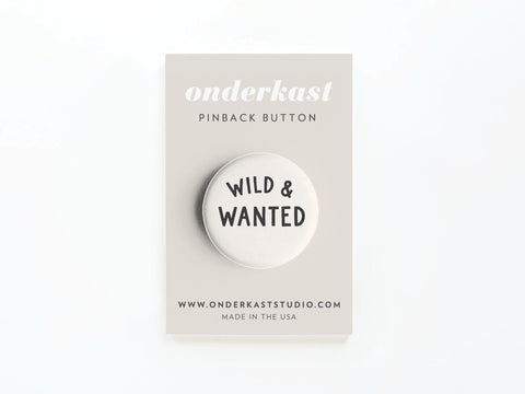 The Wild & Wanted Pinback Button by Onderkast Studio is a bold adventure accessory on an Onderkast Studio card, featuring the button, website, and MADE IN THE USA at the bottom.