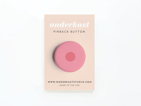 A vibrantly printed pink Nipple Pinback Button – DISCONTINUED by Onderkast Studio is attached to a beige card labeled onderkast PINBACK BUTTON, featuring www.onderkaststudio.com and Made in the USA.