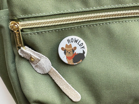 The Onderkast Studio Howldy Pinback Button shows a stylish dog in a cowboy hat and red bandana with HOWLDY text, perfect for adding playful Western flair to your green bag or accessories.