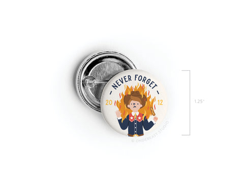 The Never Forget Pinback Button by Onderkast Studio features a cartoon girl scout with flames and a surprised look, with “NEVER FORGET” above and “2012” below—a playful Texas tribute to Big Tex’s fiery fate. Measures 1.25.