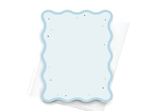 The TS 1989 Wavy Die Cut Notecard by Onderkast Studio, featuring black and gold star details on light blue, brings Swiftie charm to your desk when placed atop a crisp white folded napkin.