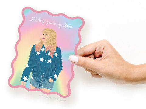 A hand holds the TS Lover Wavy Die Cut Notecard by Onderkast Studio, featuring a pastel wavy design with an illustrated woman in a fringed, star-patterned jacket and “Darling, you’re my Lover” at the top—a nod to Taylors iconic song.