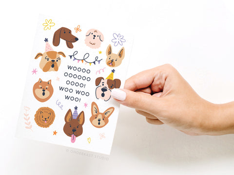 A hand holds the Woo! Birthday Dogs Greeting Card by Onderkast Studio, featuring fun dog breed illustrations with colorful doodles and “WOOOOO! OOOO! OOOO! WOO WOO WOO!” in the center—a perfect card for dog lovers.