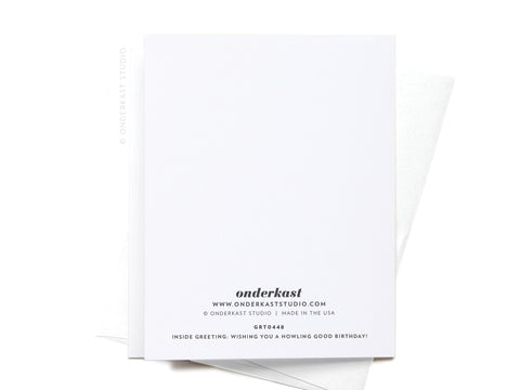 The back of a white Woo! Birthday Dogs Greeting Card by Onderkast Studio sits on a matching envelope, showing the brand and website. Inside message: Wishing you a howling good birthday! Ideal for dog lovers and fans of cute dog art.